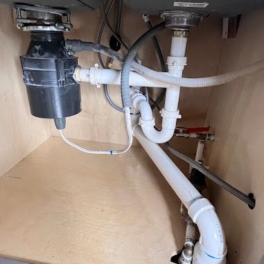 Under-sink cabinet with a garbage disposal, white PVC drain lines, and a dishwasher line