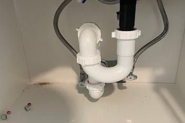 New white PVC p-trap and drain under a bathroom vanity with braided supply lines