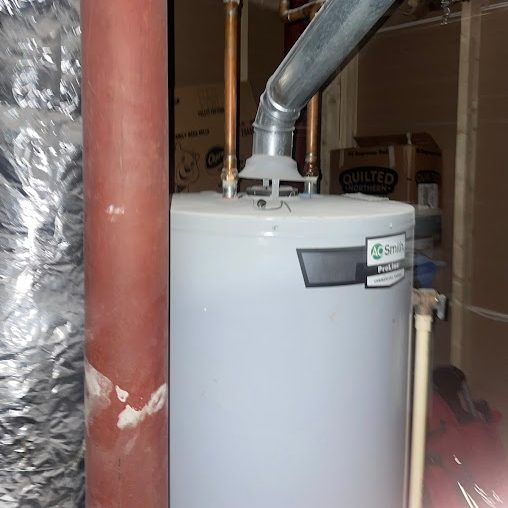 Blue-gray tank water heater beside a rust-red pipe and a foil-wrapped duct in a basement utility space