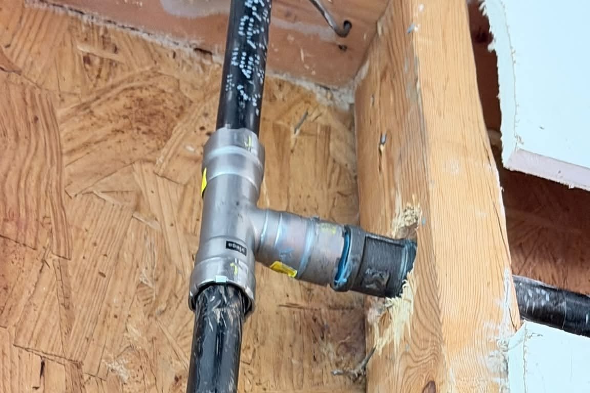Black gas pipe with a press fitting tee inside an opened wall frame