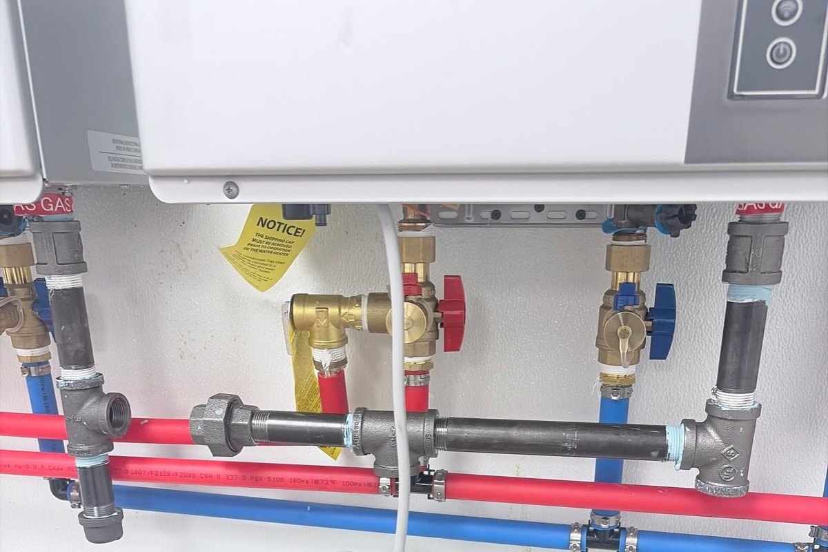 Wall-mounted tankless water heater with black iron gas piping, shutoff valves, and red and blue PEX lines