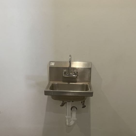 Small stainless steel hand sink with a p-trap mounted on a white wall