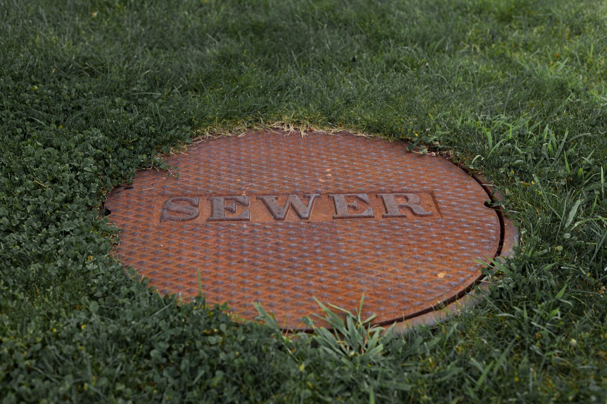 Rusty cast iron sewer access cover set flush in a green lawn