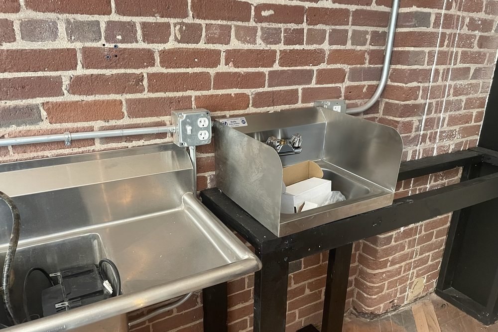 Stainless steel sinks on a black stand against a brick wall