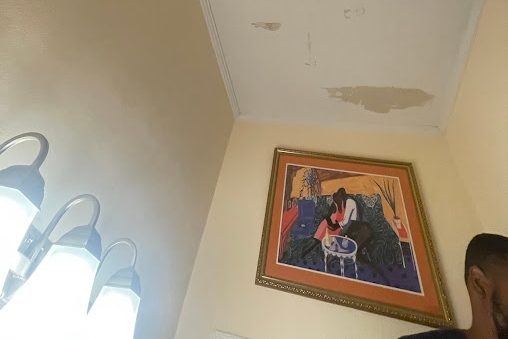 Ceiling of a small room with several peeling water stains and a framed painting at the side