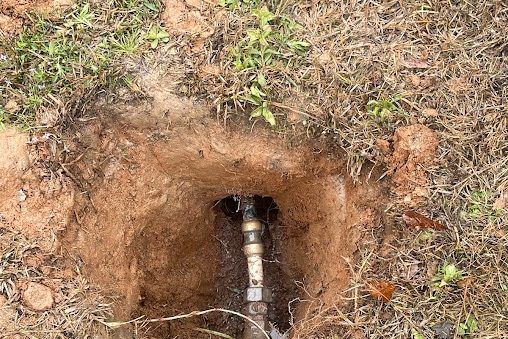 Small hole in a lawn exposing a brass fitting on a buried water pipe