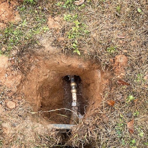 Small hole in a lawn exposing a brass fitting on a buried water pipe