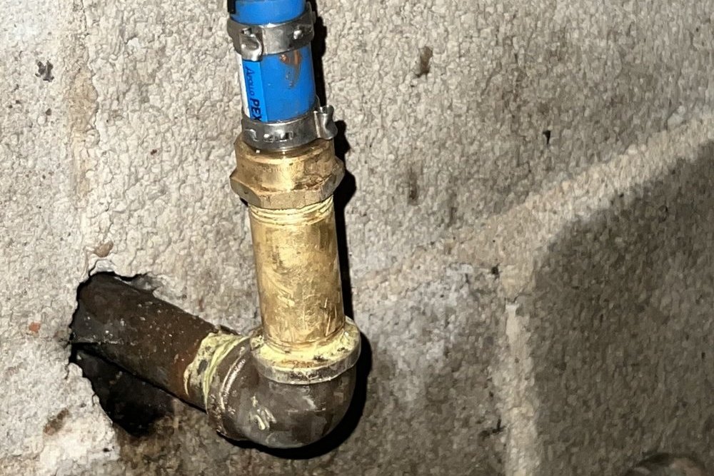 Blue PEX with a clamp ring joined to a brass fitting and black iron elbow on a rough wall