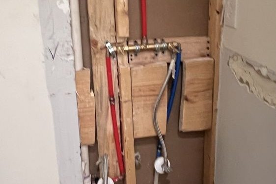 Opened wall with a red PEX line and a white pipe between bare studs