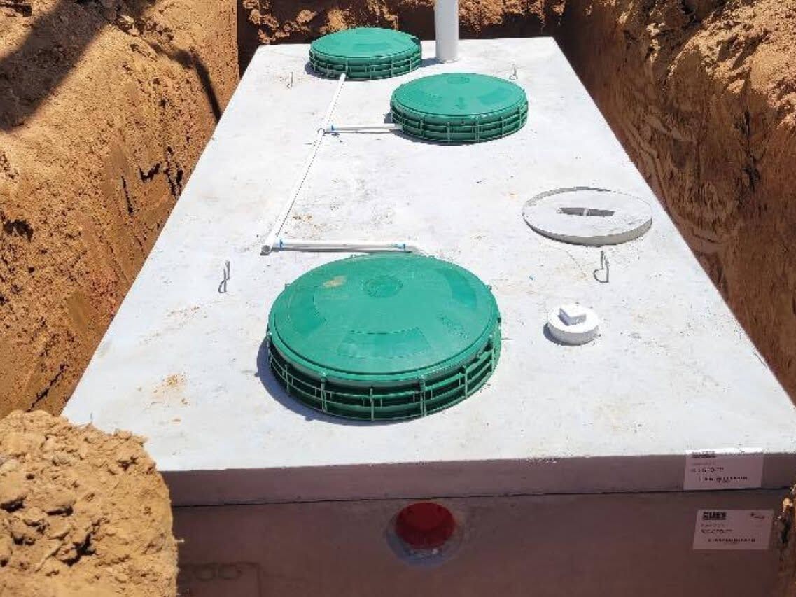 New concrete septic tank with green riser lids set in an open excavation