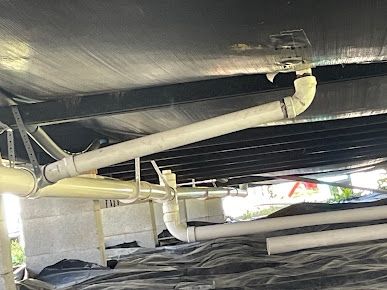 White PVC and iron drain lines hanging in a crawlspace
