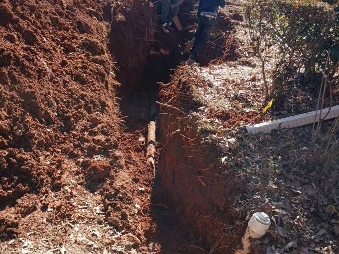Two workers at the far end of a deep red clay trench