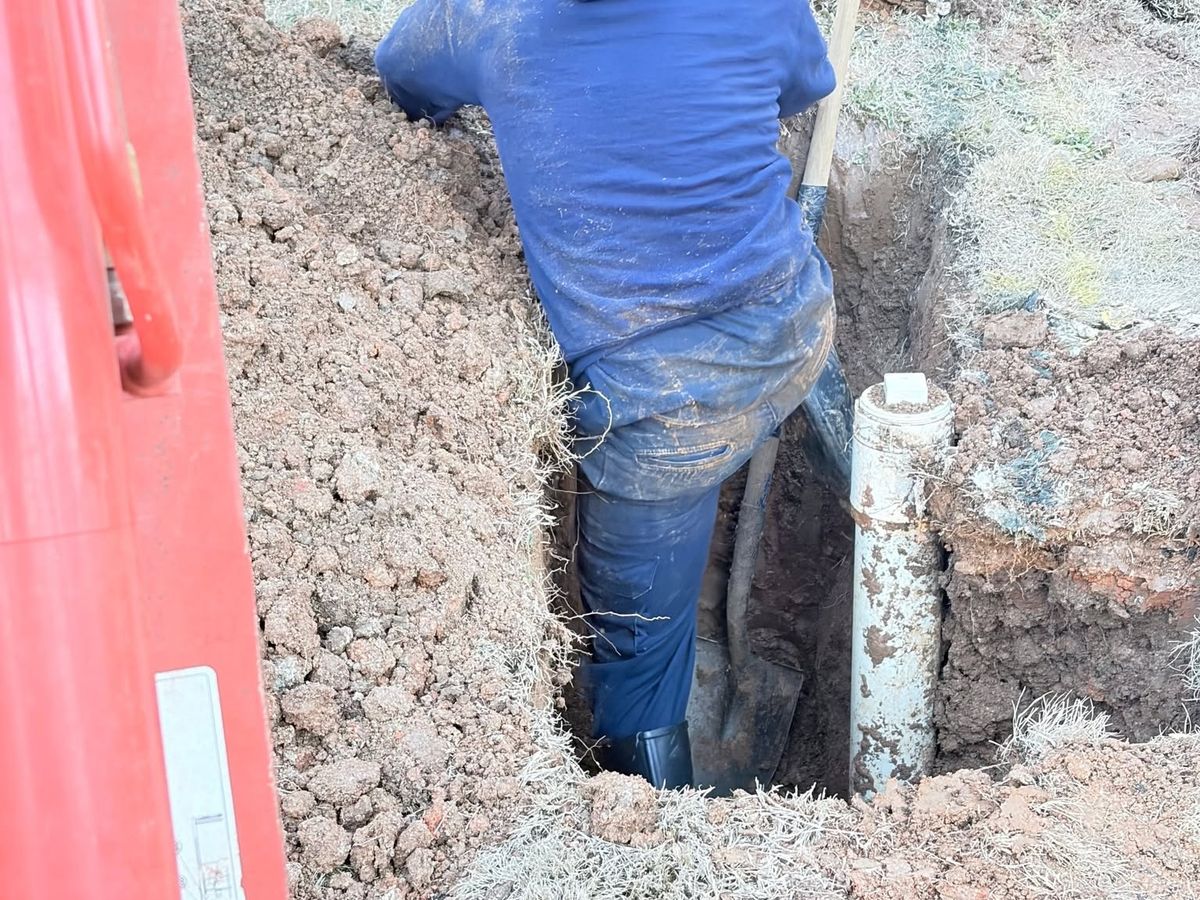 Worker in a trench beside a white vertical PVC pipe