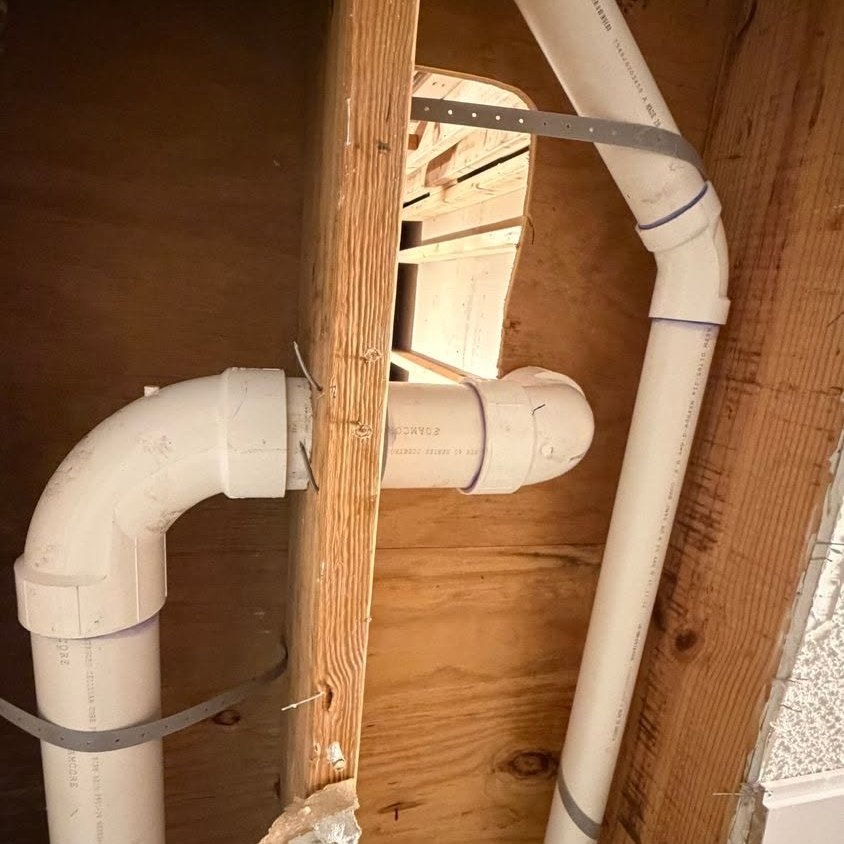 PVC drain pipes with elbows strapped inside an opened wall cavity