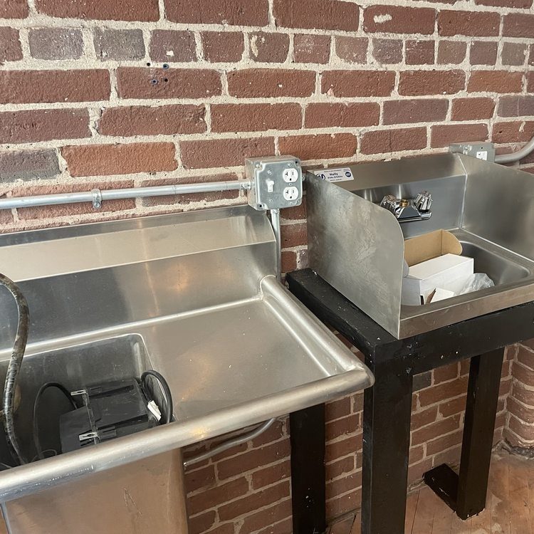 Stainless steel sinks on a black stand against a brick wall