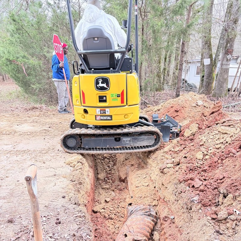 Yellow mini excavator parked over an open trench on a rural road