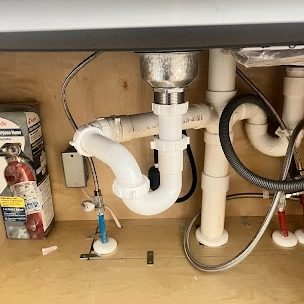 White PVC p-trap and drain lines under a kitchen sink cabinet with braided supply lines