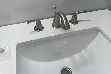 Brushed nickel three-piece faucet on a white vanity top with an undermount sink
