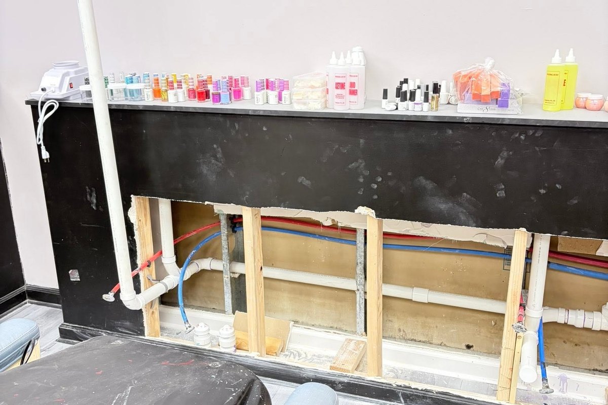 Salon wall opened at the base with new drain and supply piping beside a pedicure chair