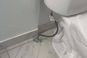 Base of a new white toilet with a braided supply line on a marble-look tile floor