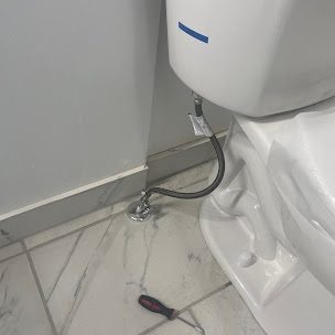 Base of a new white toilet with a braided supply line on a marble-look tile floor