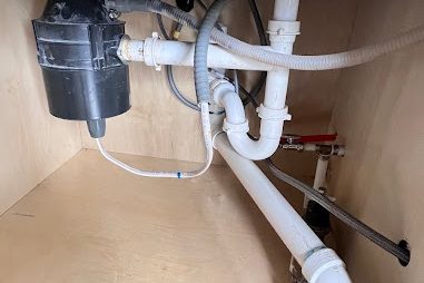 Under-sink cabinet with a garbage disposal, white PVC drain lines, and a dishwasher line