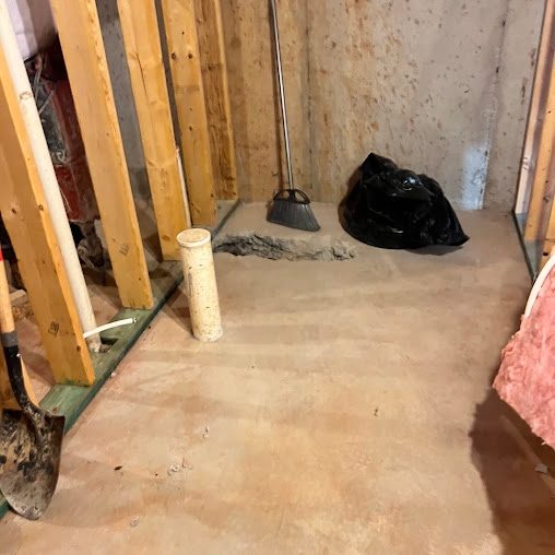 Framed basement room with a white drain pipe stub in a trench cut in the concrete floor