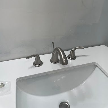 Brushed nickel three-piece faucet on a white vanity top with an undermount sink