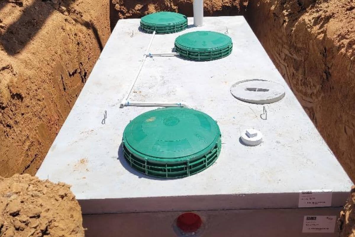 New concrete septic tank with green riser lids set in an open excavation