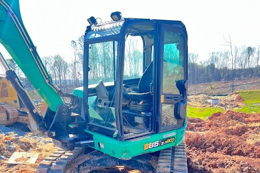 Green tracked excavator parked on a mound of red clay on a cleared building lot