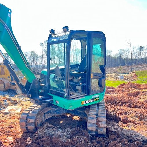 Green tracked excavator parked on a mound of red clay on a cleared building lot