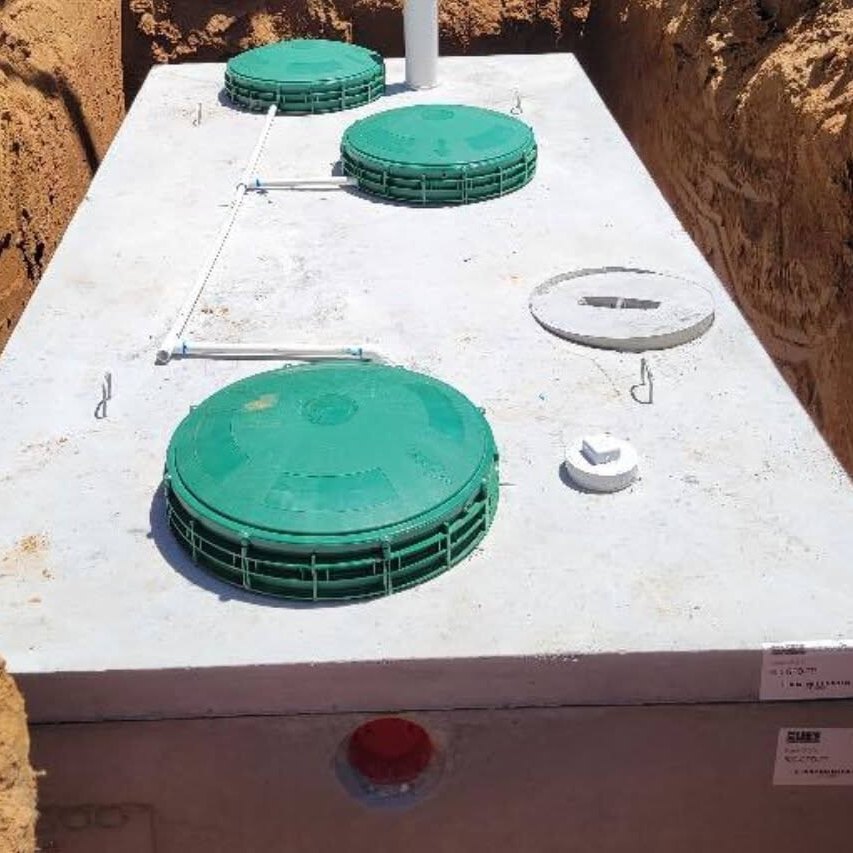 New concrete septic tank with green riser lids set in an open excavation