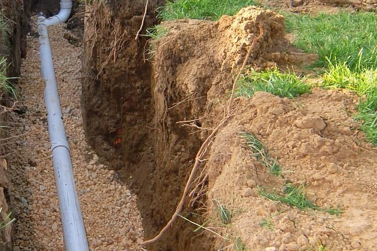 Gray pipe in a gravel bed in a drain field trench beside an open dirt trench