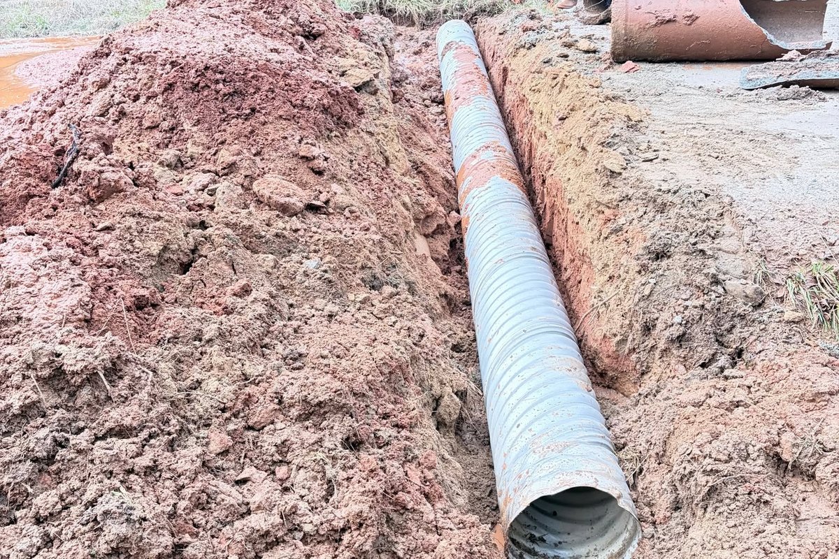 Large corrugated pipe lying in a red clay trench