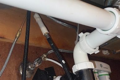 White PVC drain and slip joints under a sink with braided supply lines