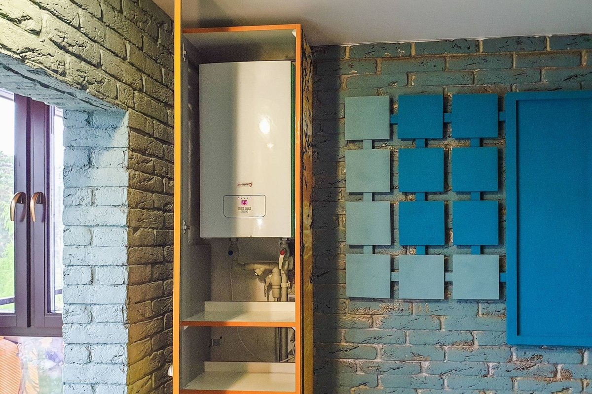 White wall-mounted water heater inside an open cabinet with pipes and valves below it