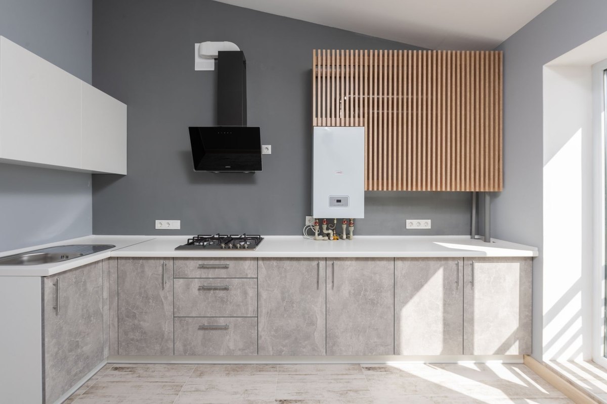White wall-mounted water heater with pipes and valves beneath it in a modern gray kitchen