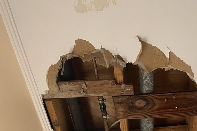 Torn hole exposing joists and a pipe in a hallway