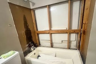 Bathroom wall opened behind a tub showing a dark water stain on the wall board