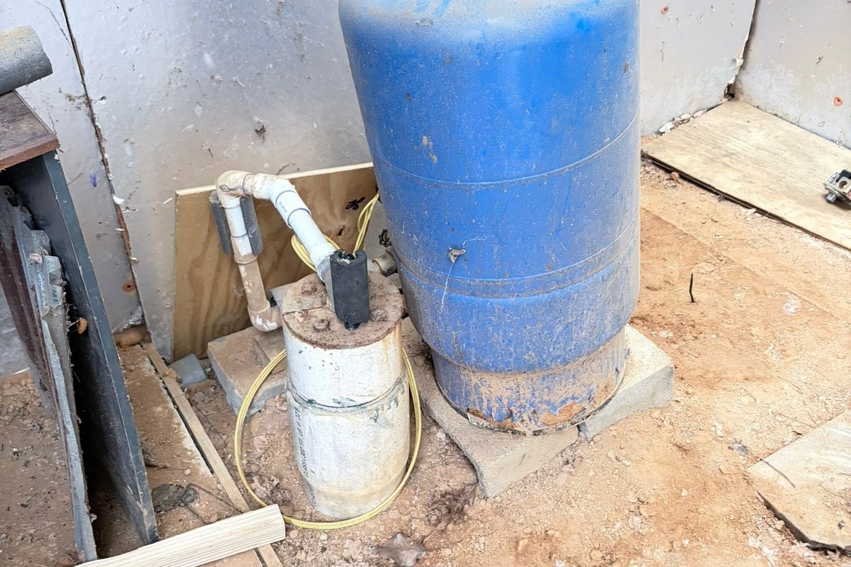 Old blue pressure tank and well pump housing on a dirt floor in an unfinished building