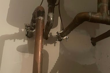 Copper water lines with brackets running along a gray wall