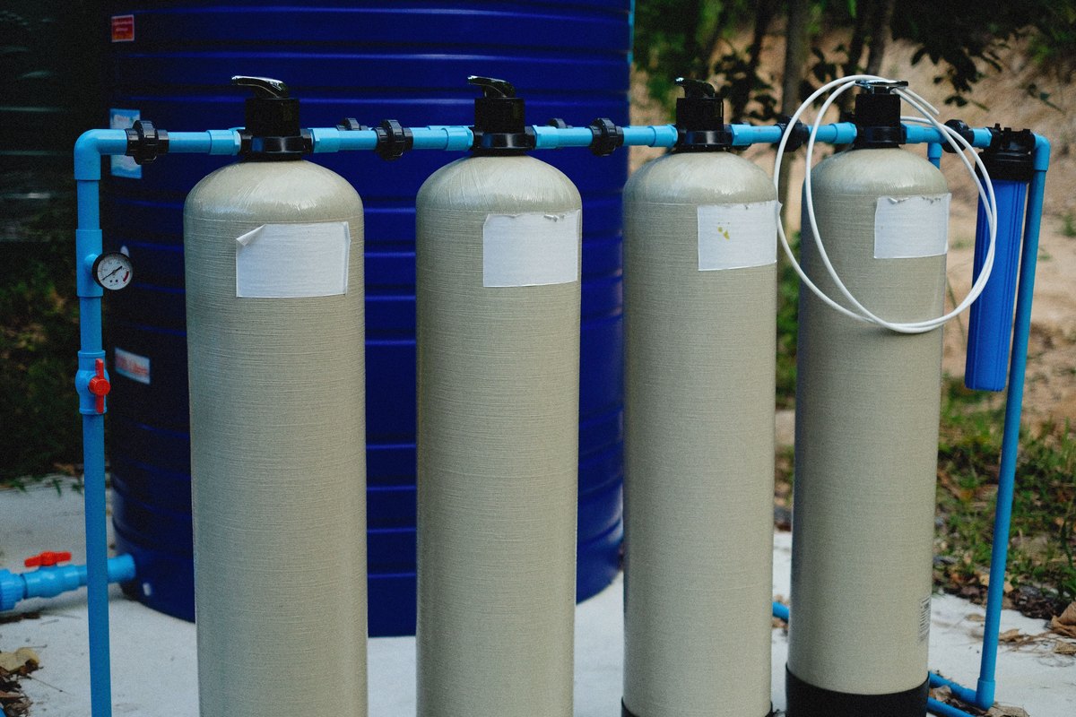 Four beige water treatment tanks with black valves joined by blue piping