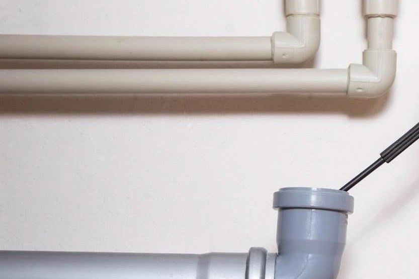 Clean mock-up of beige PVC supply pipes and a gray drain elbow on a white wall