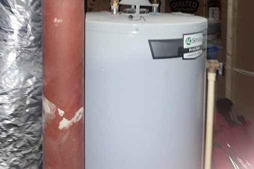 Blue-gray tank water heater beside a rust-red pipe and a foil-wrapped duct in a basement utility space