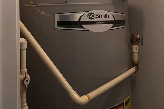 Gray tank water heater with a cream CPVC pipe and brass fittings in a closet
