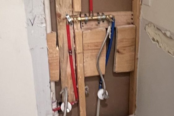 Landscape view of an opened wall with red PEX and a white pipe between bare studs